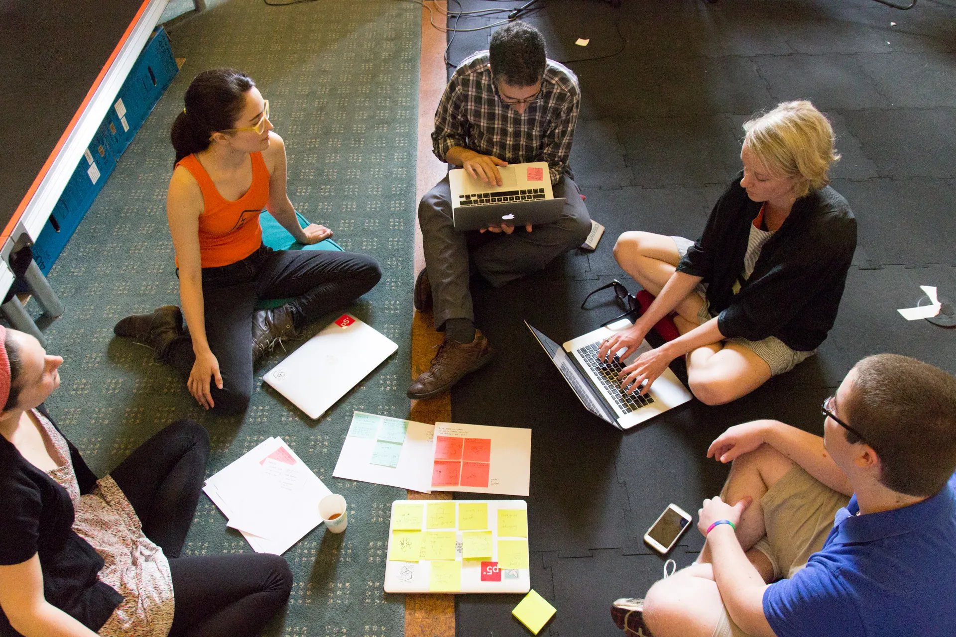 Five people in a circle with their laptops sharing their notes