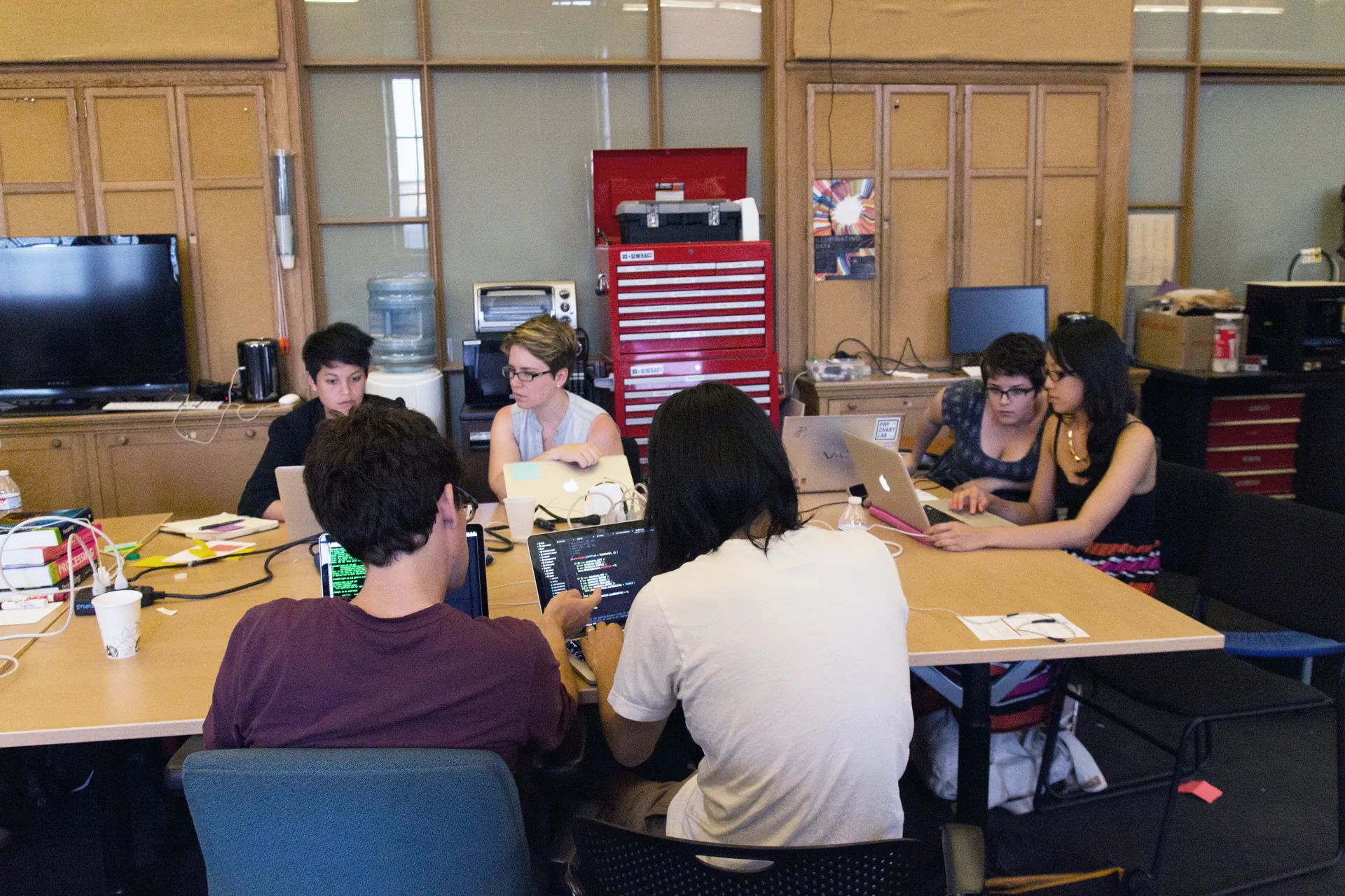 Participants sit around a table looking at each others laptops and compare code