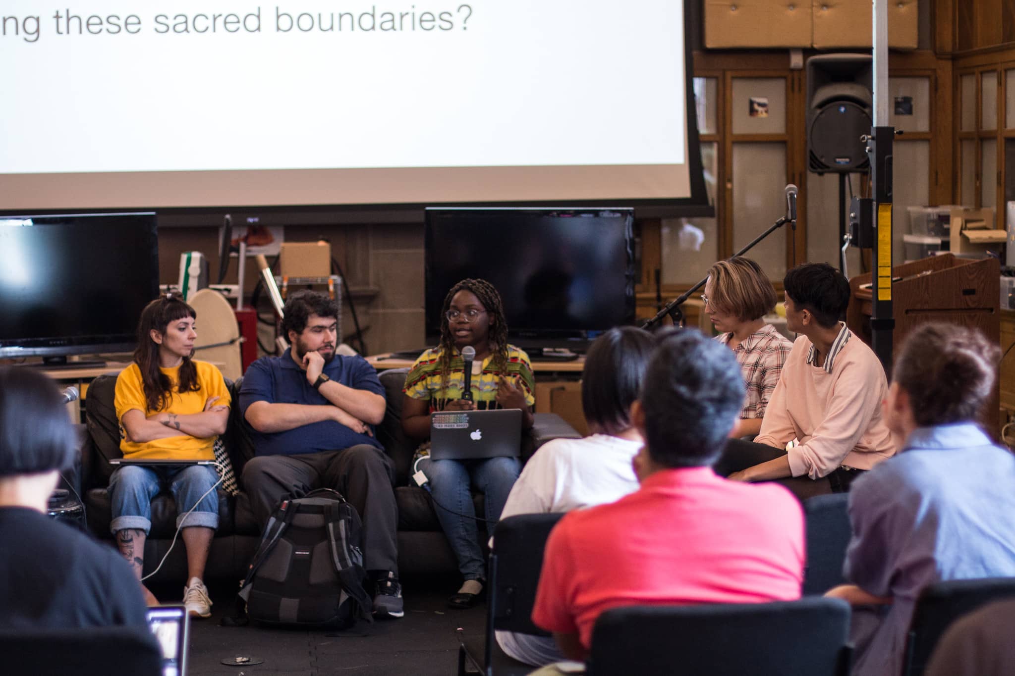 Woman with microphone speaking to fellow participants with the text sacred boundaries in the projection behind her