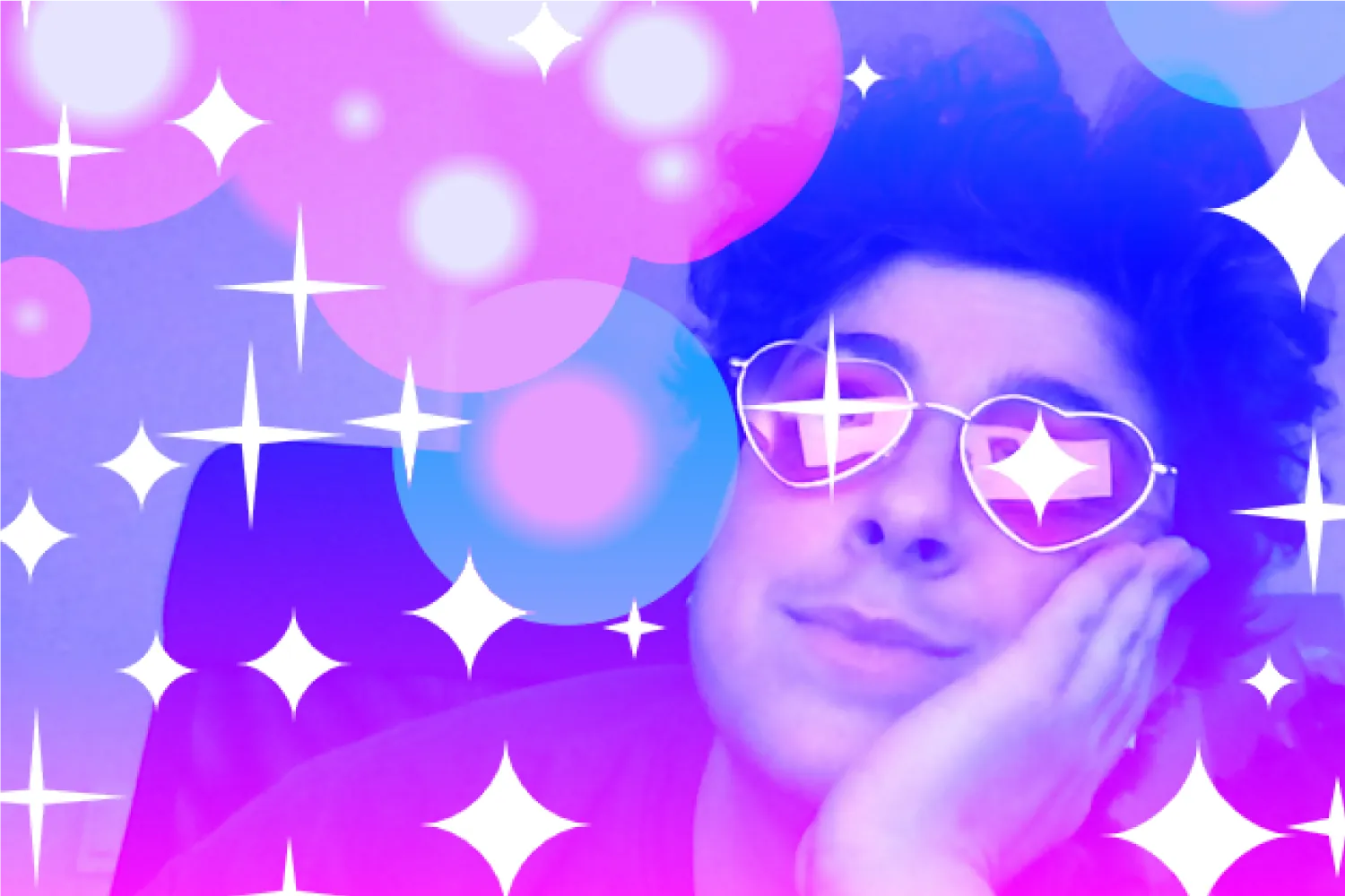 A white person with short, dark curly hair wears pink heart-shaped glasses and a dark sleeveless shirt. He places his hand on his cheek and looks diagonally to the left, smiling softly. A vertical linear blue to pink gradient is overlaid. On top of that, we see a mixture of angular and curved white 4-pointed sparkles of varying sizes, with an angular sparkle over the left lens of his glasses, and a curved sparkle over the right lens. We see pink and blue radial gradient circles layered on top, creating a lens flare effect.