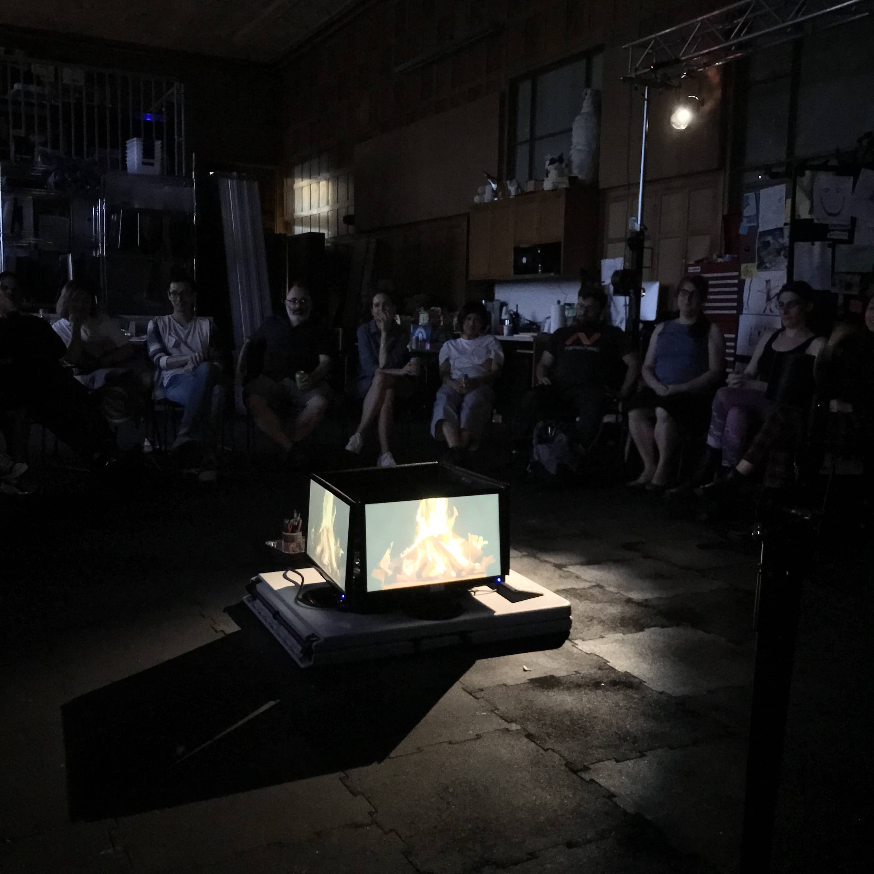 Group of people sit around campfire made from four LCD monitors.