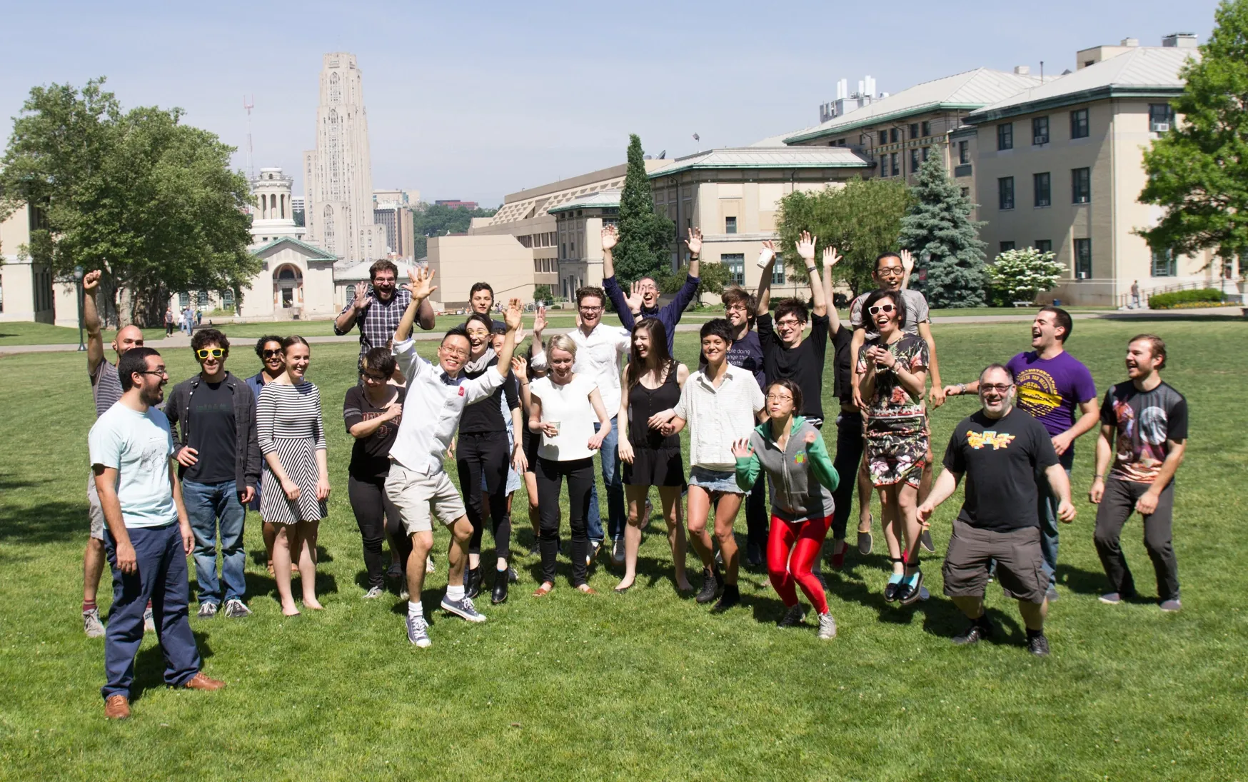 Participants jump, smile and throw their hands in the air on a green lawn.